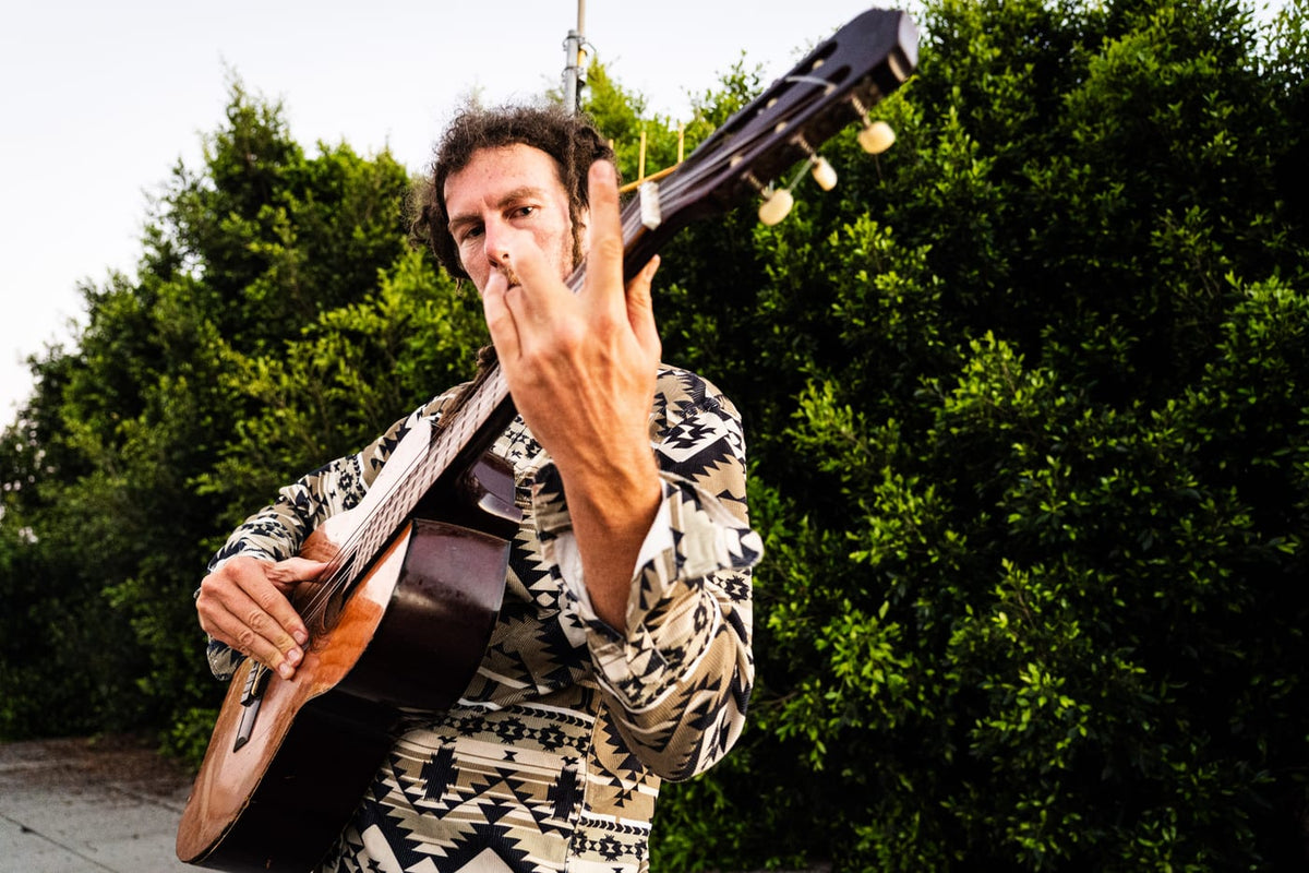 Man in Aztec-print shirt holding guitar and blowing a kiss outdoors