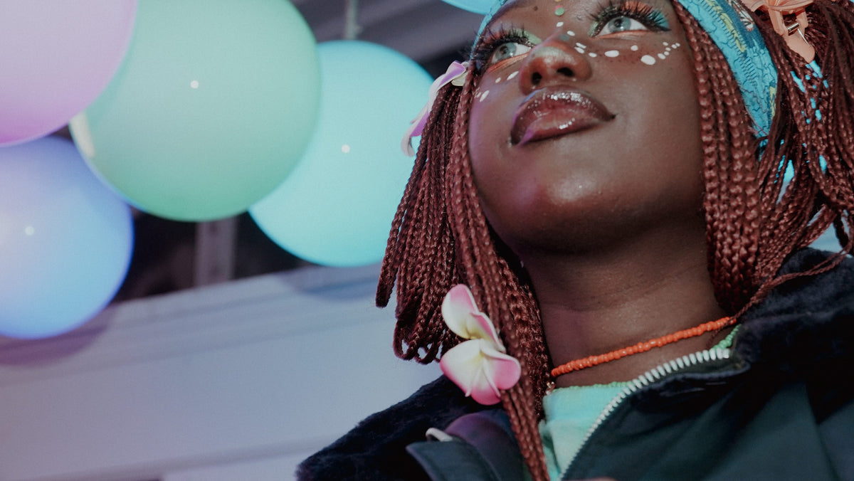 Close-up portrait with braids, festival face paint, plumeria flowers, and pastel balloons