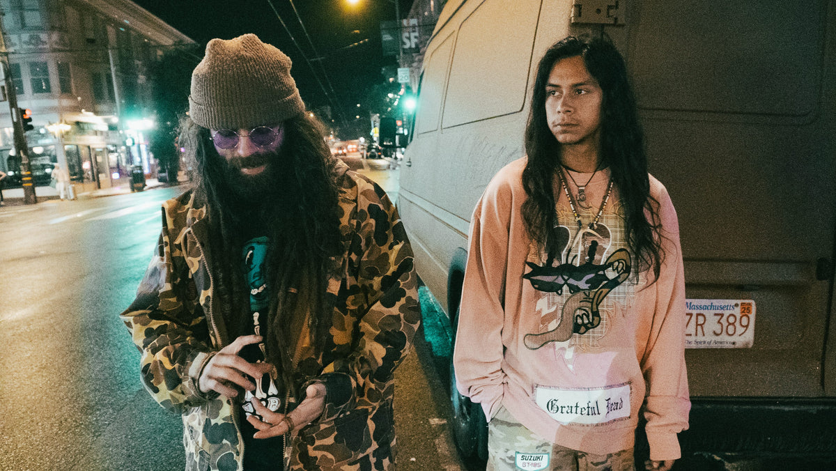 Two men on a city street at night in camo jacket and pink Grateful Dead sweatshirt
