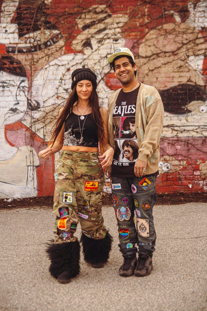 Couple posing in front of red street mural in patched camo pants and Beatles tee with patched jeans