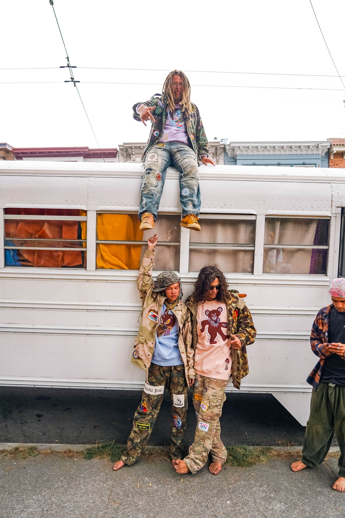 Crew posing by the tour bus with one standing on top and two below in Further gear