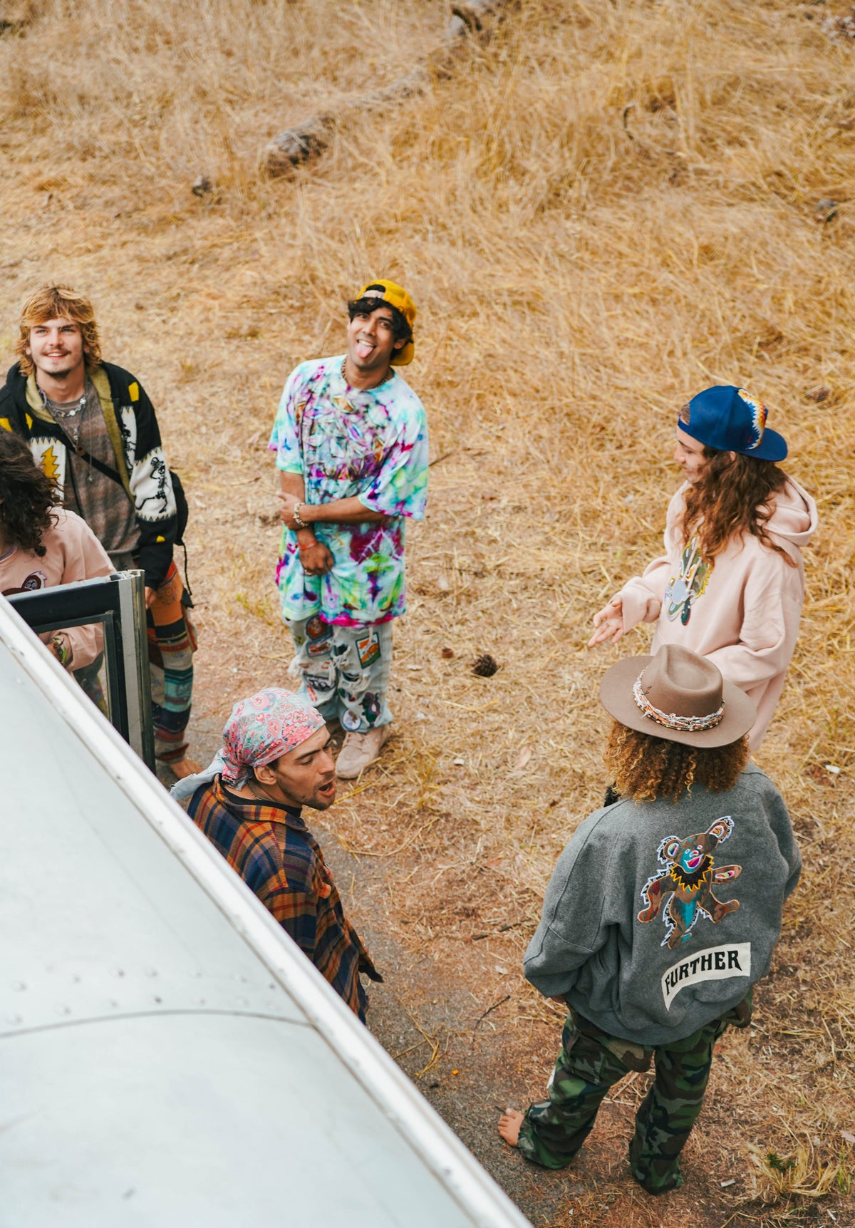Group of friends hanging out by a bus on a golden hillside wearing Further branded pieces