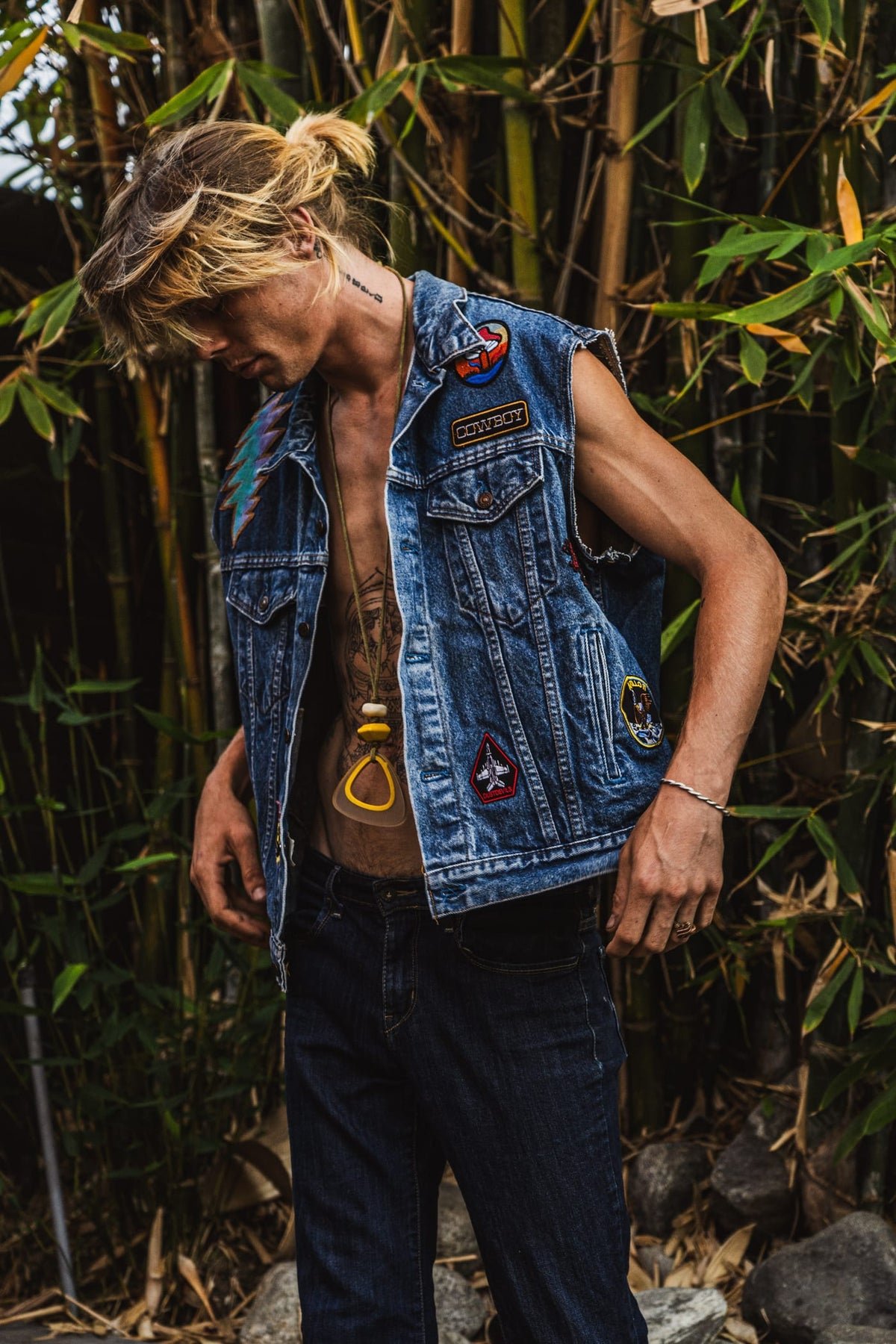 Man in patched denim vest with vintage pins standing among bamboo