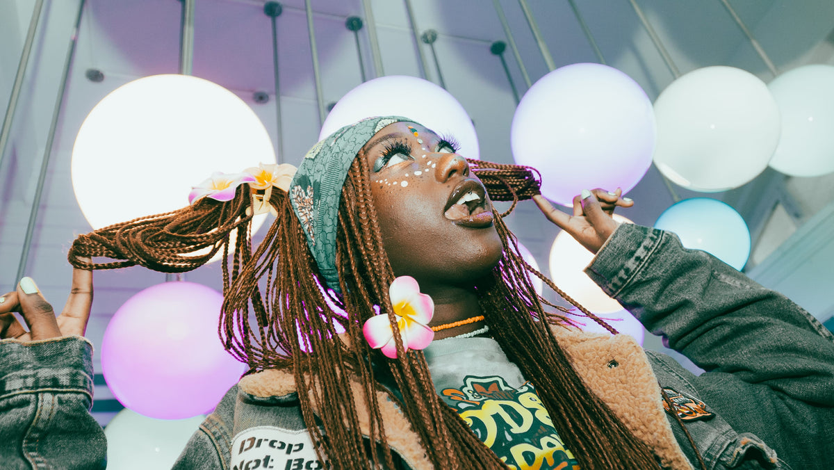 Woman posing under purple-lit globe lights in sherpa denim jacket with plumeria in hair