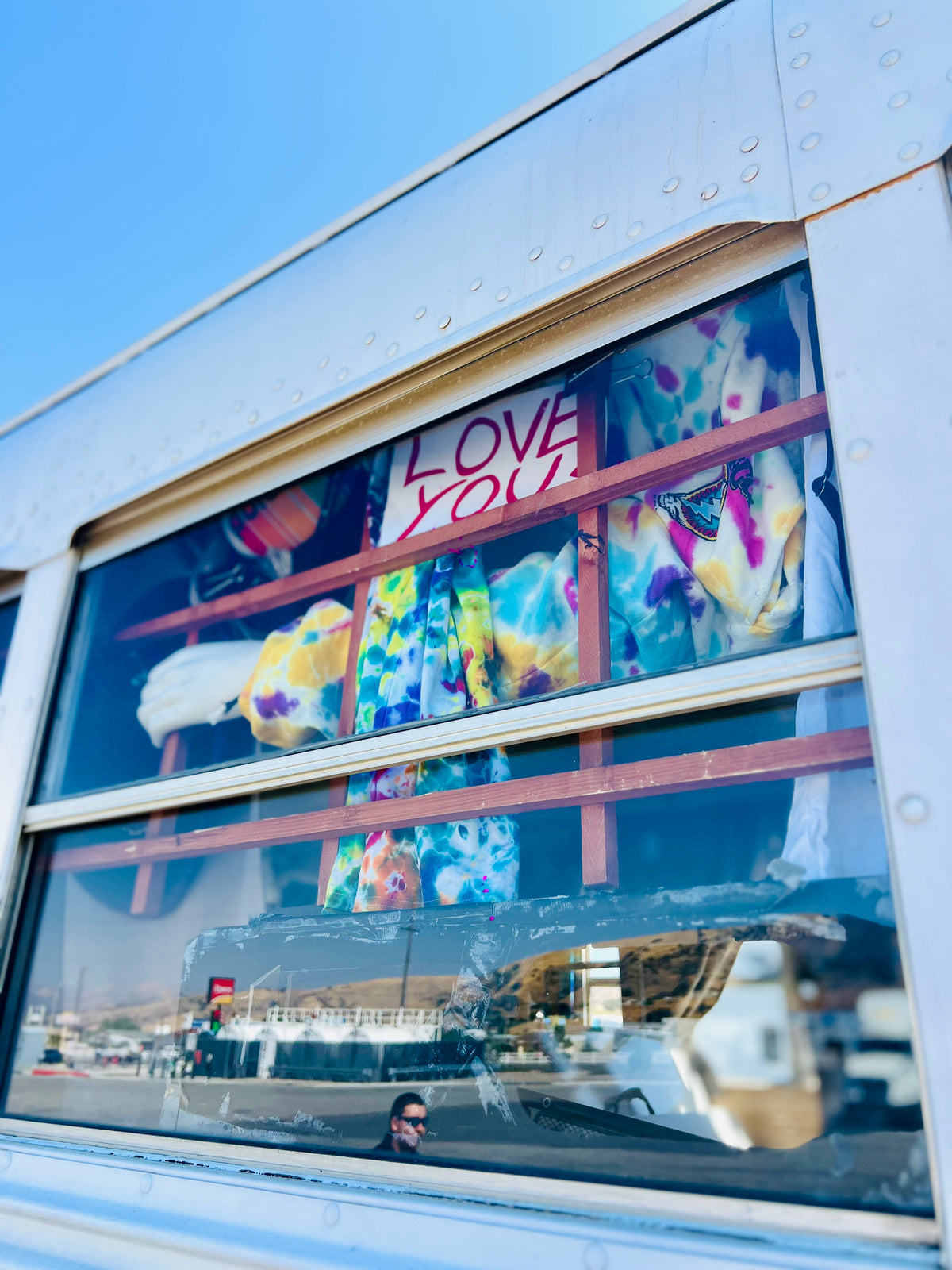 Bus window displaying tie-dye clothing with a Love You sign