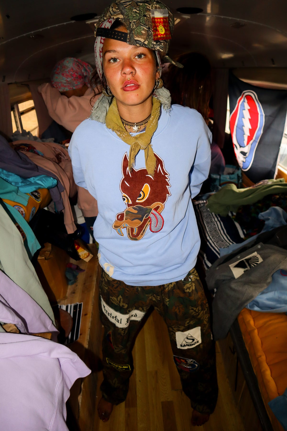 Woman in light blue sweatshirt with wolf graphic inside the bus wearing camo pants and hunting cap